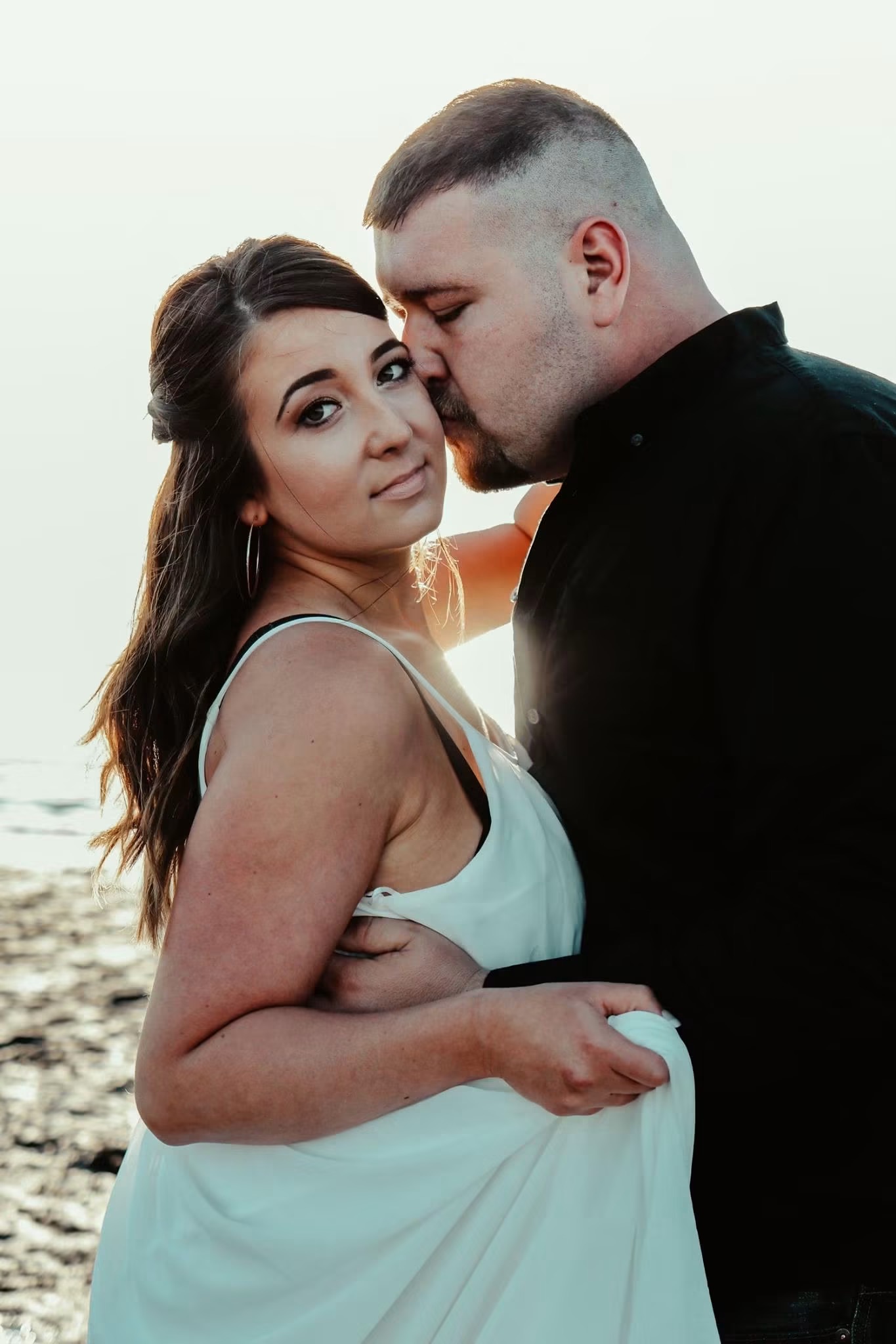 A newly engaged couple embracing on the beach at sunset