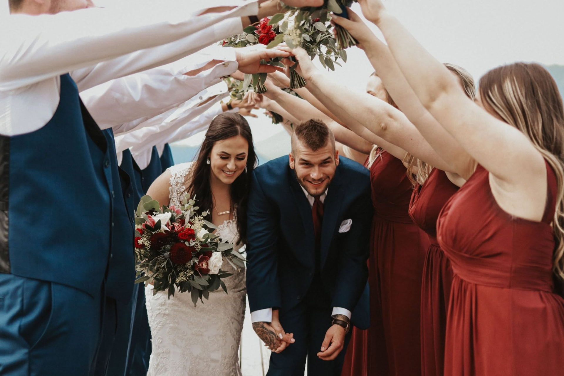 Newlyweds walking beneath an arch of bouquets held by their wedding party