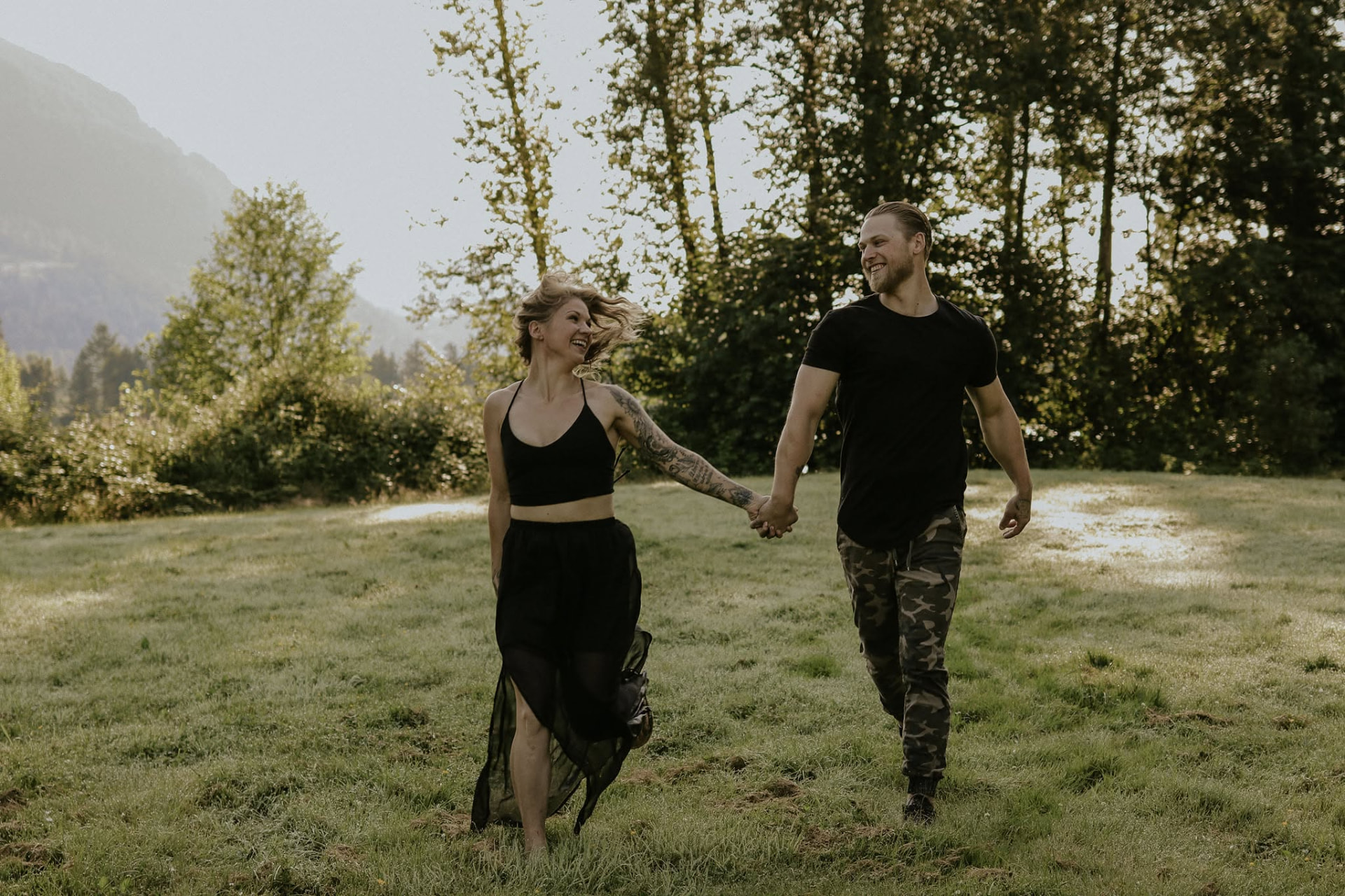 Couple walking hand in hand through a sunlit field — McManus Photography
