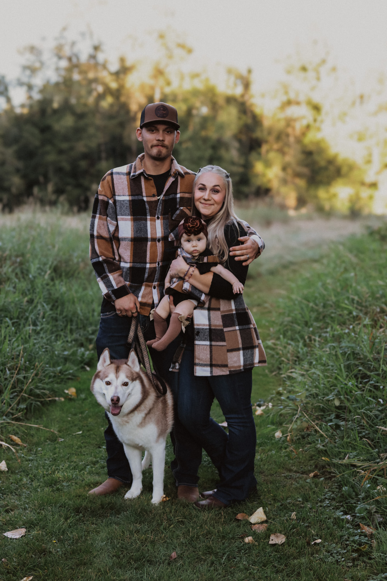 Family in plaid with their baby and husky in a grassy field
