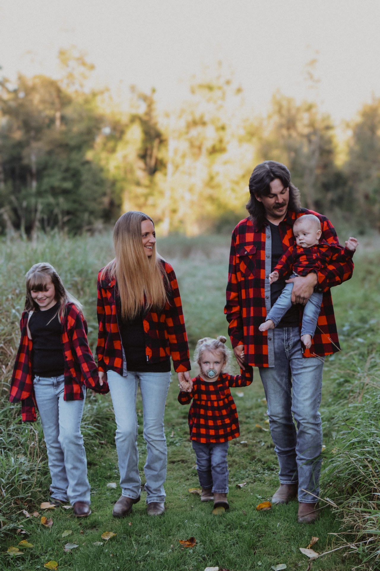 Family of five in matching red plaid walking a grassy path