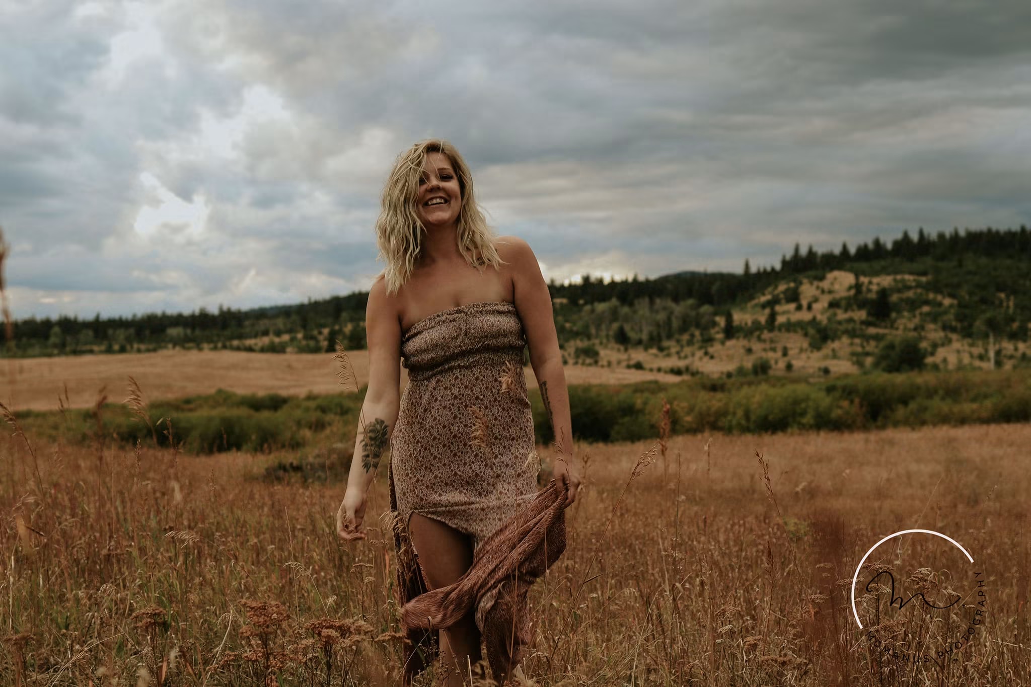 Portrait of a woman walking through a golden field beneath dramatic clouds — McManus Photography