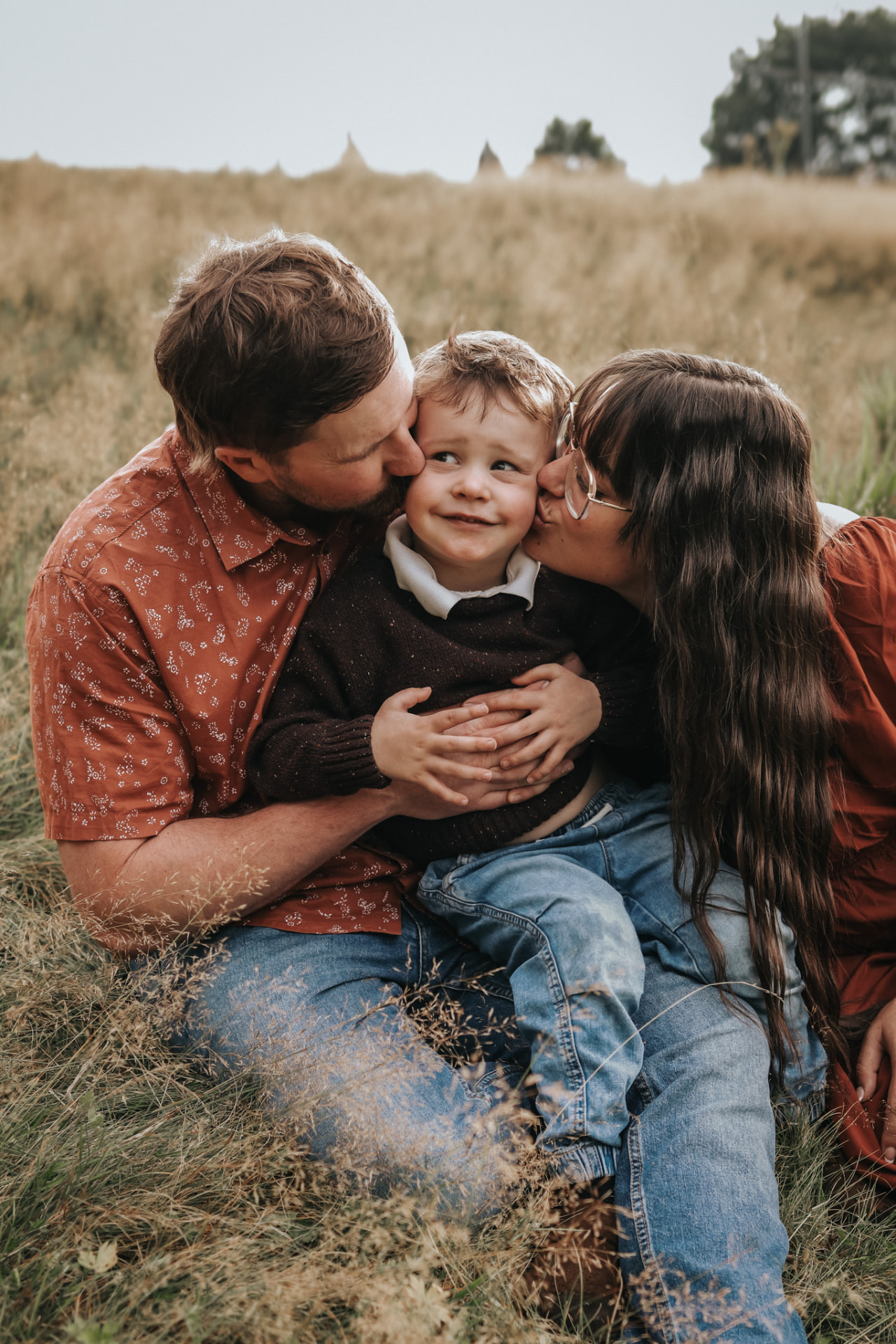 Parents kissing their son on both cheeks in a field