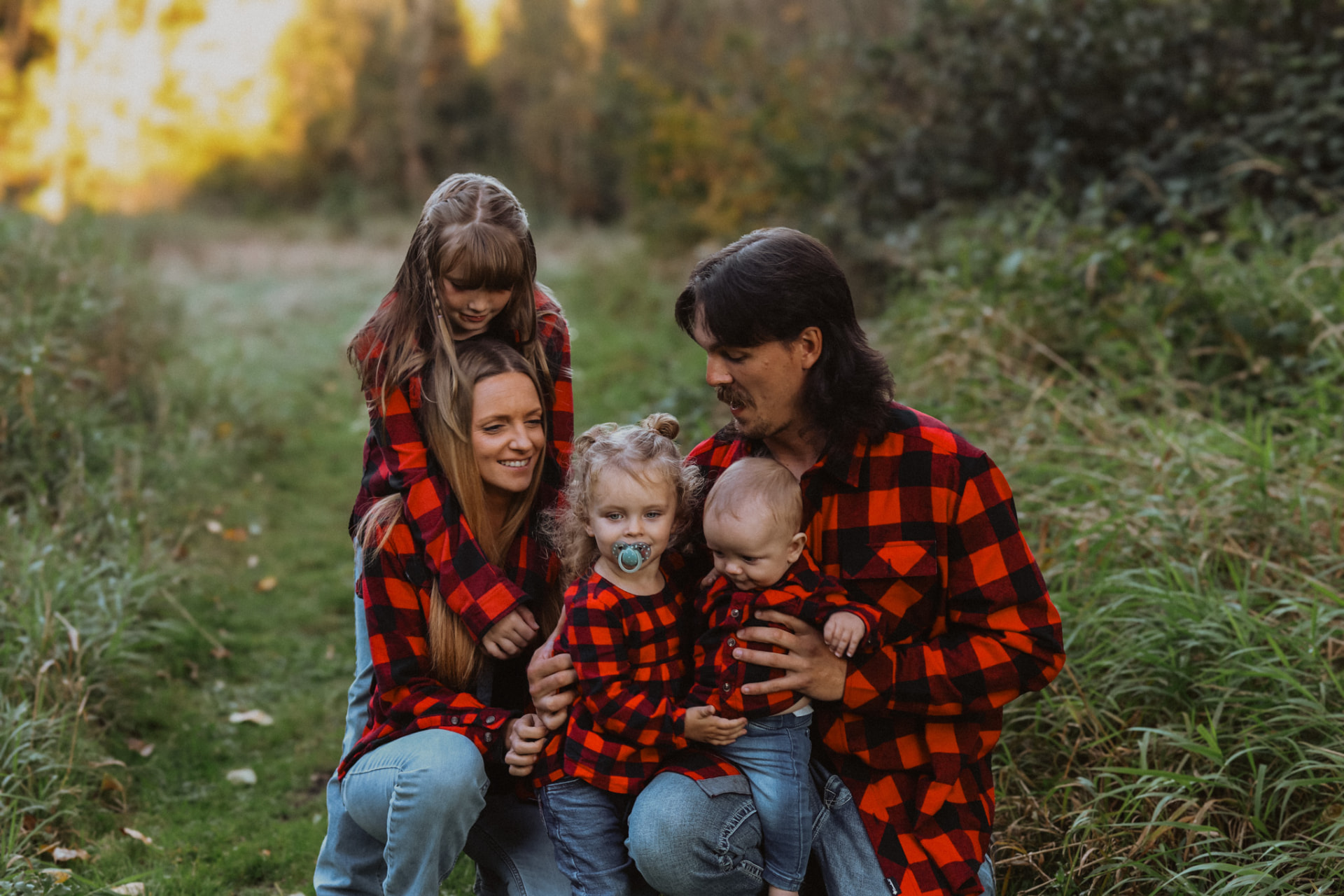 Family of five in red plaid huddled together at golden hour