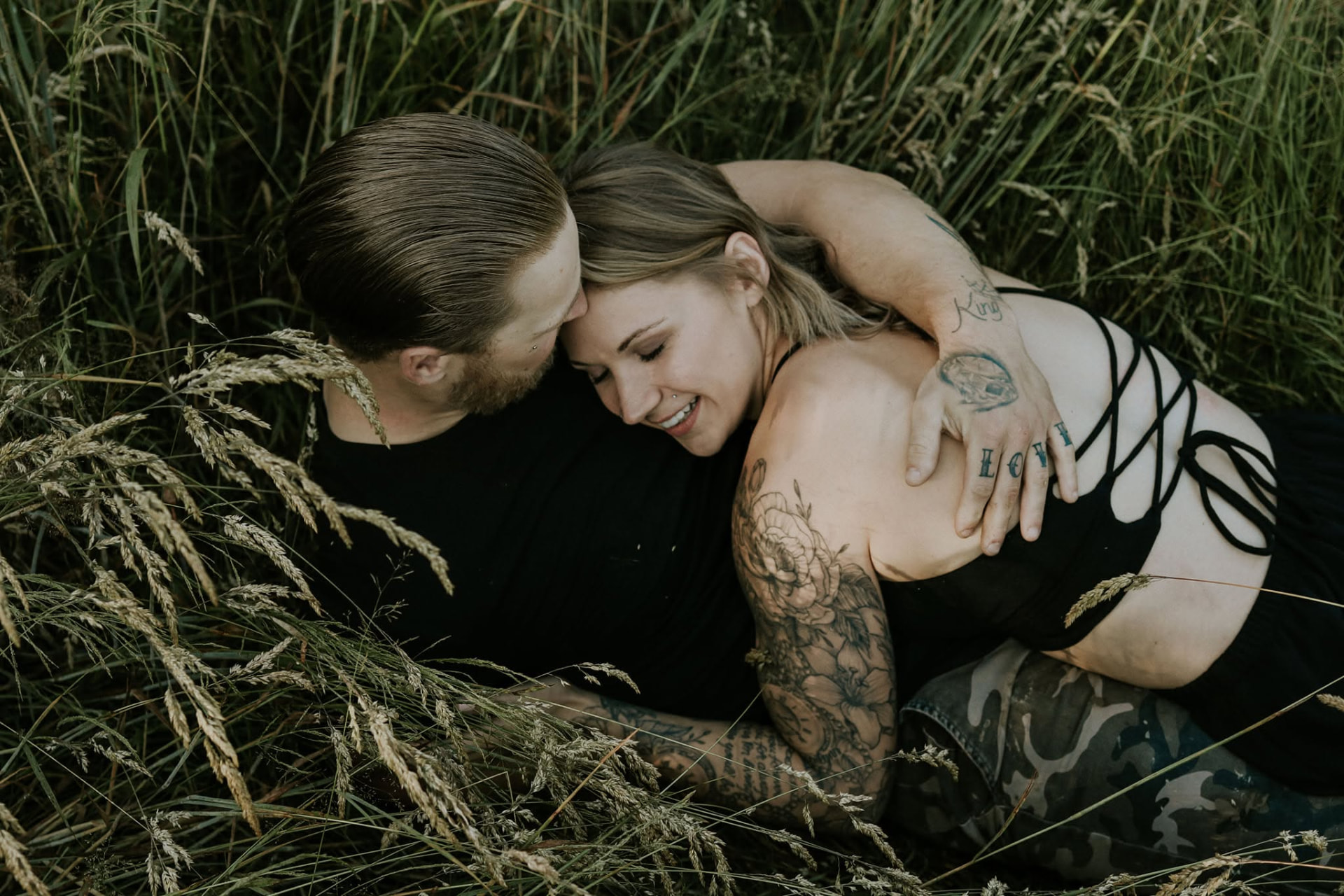 Couple lying in tall grass, foreheads together, laughing — McManus Photography