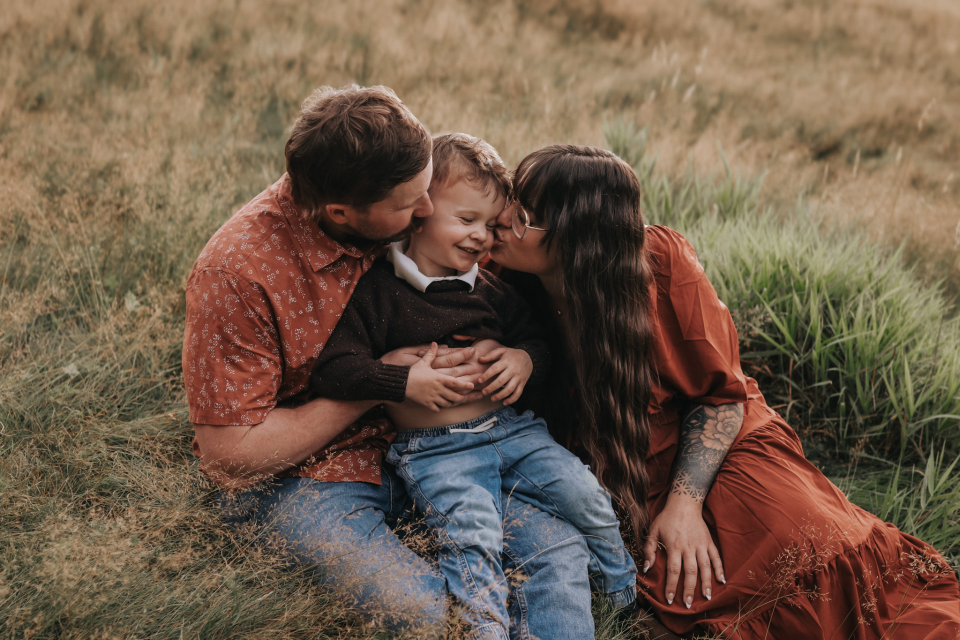 Parents kissing their laughing son in tall grass