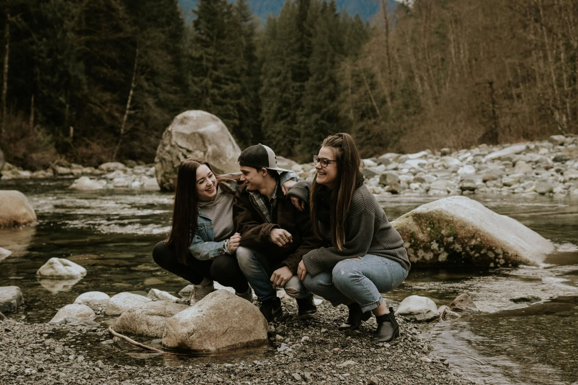 Siblings crouched by a mountain river, laughing — McManus Photography