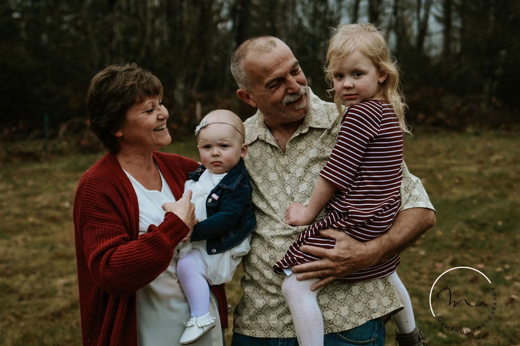 Grandparents holding their two young grandchildren at the edge of the woods
