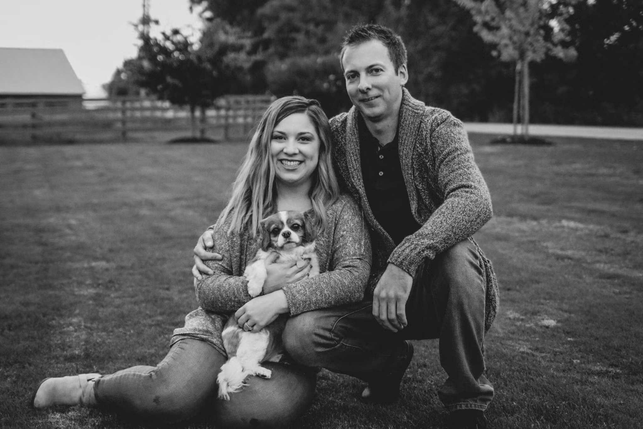 Black and white portrait of a couple sitting in the grass with their small dog