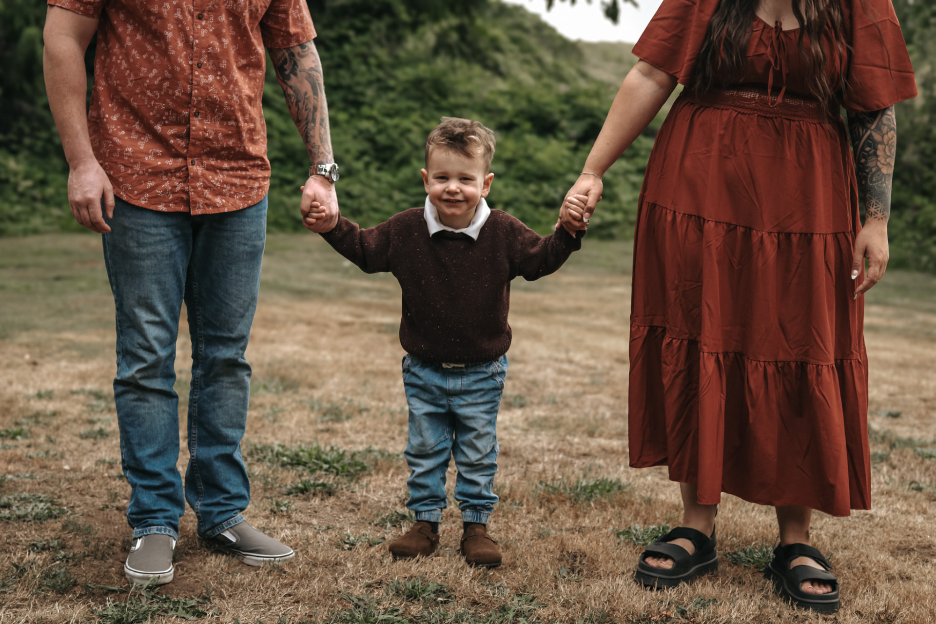 Little boy holding both parents hands in a meadow