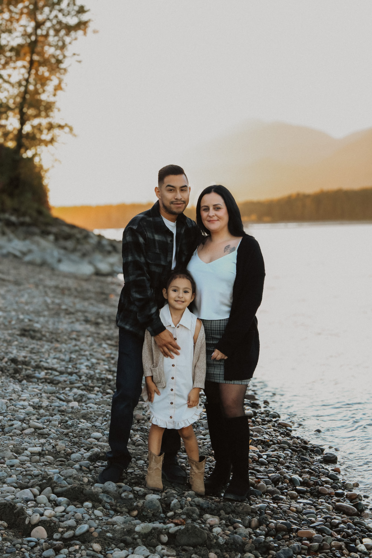 Family of three standing on a pebble shore at sunset