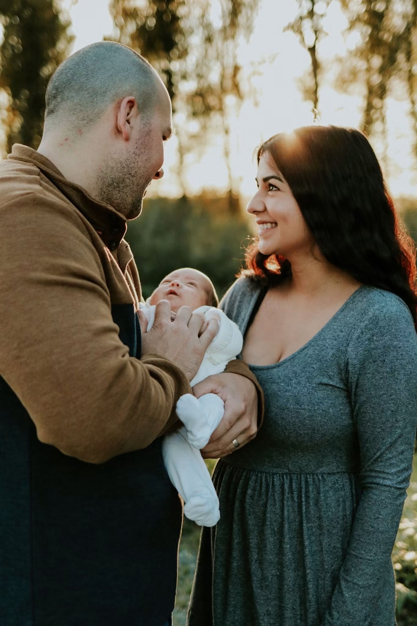 New parents looking at each other while holding their newborn at sunset