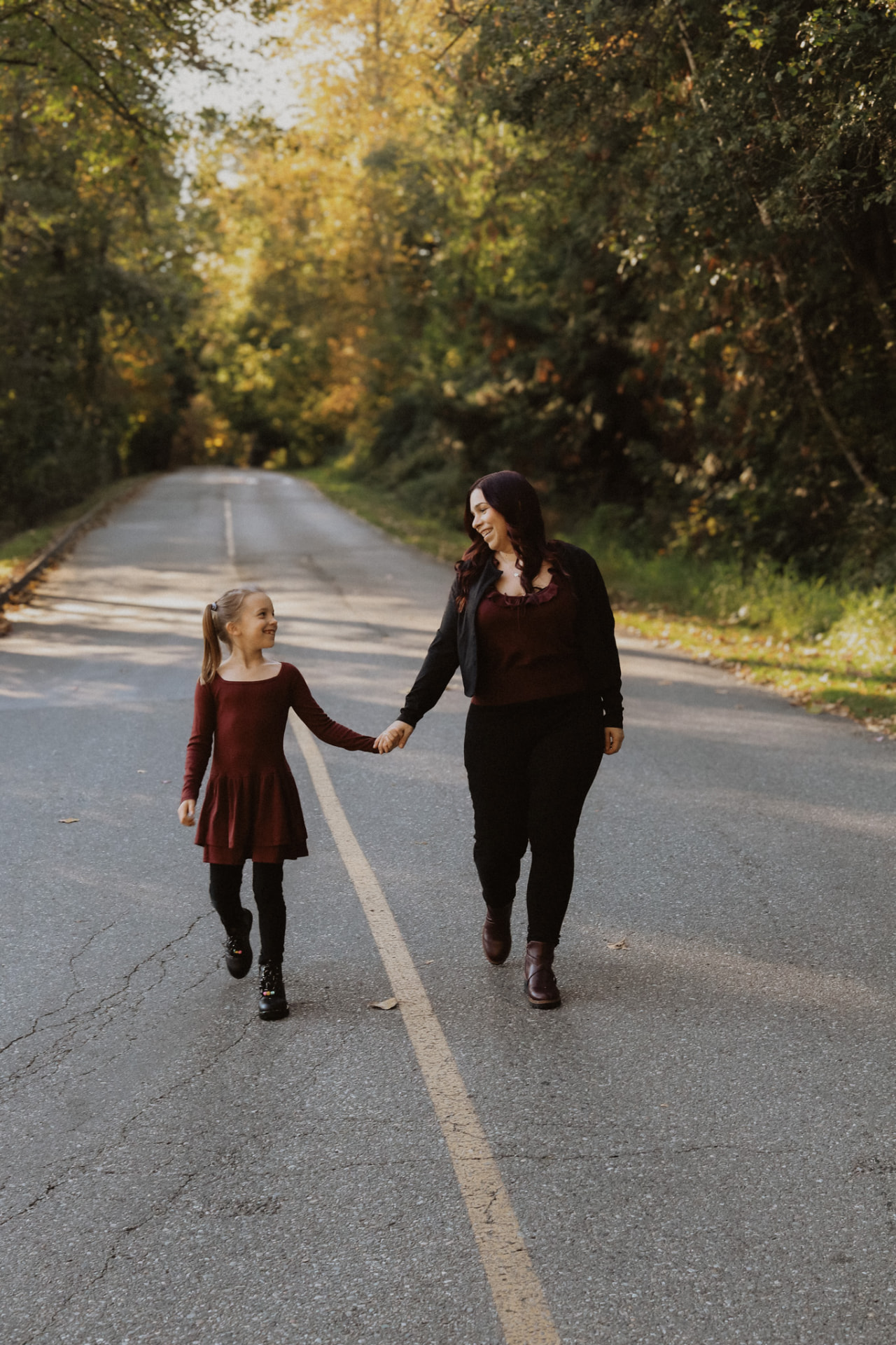 Mother and daughter walking hand in hand down a tree-lined road