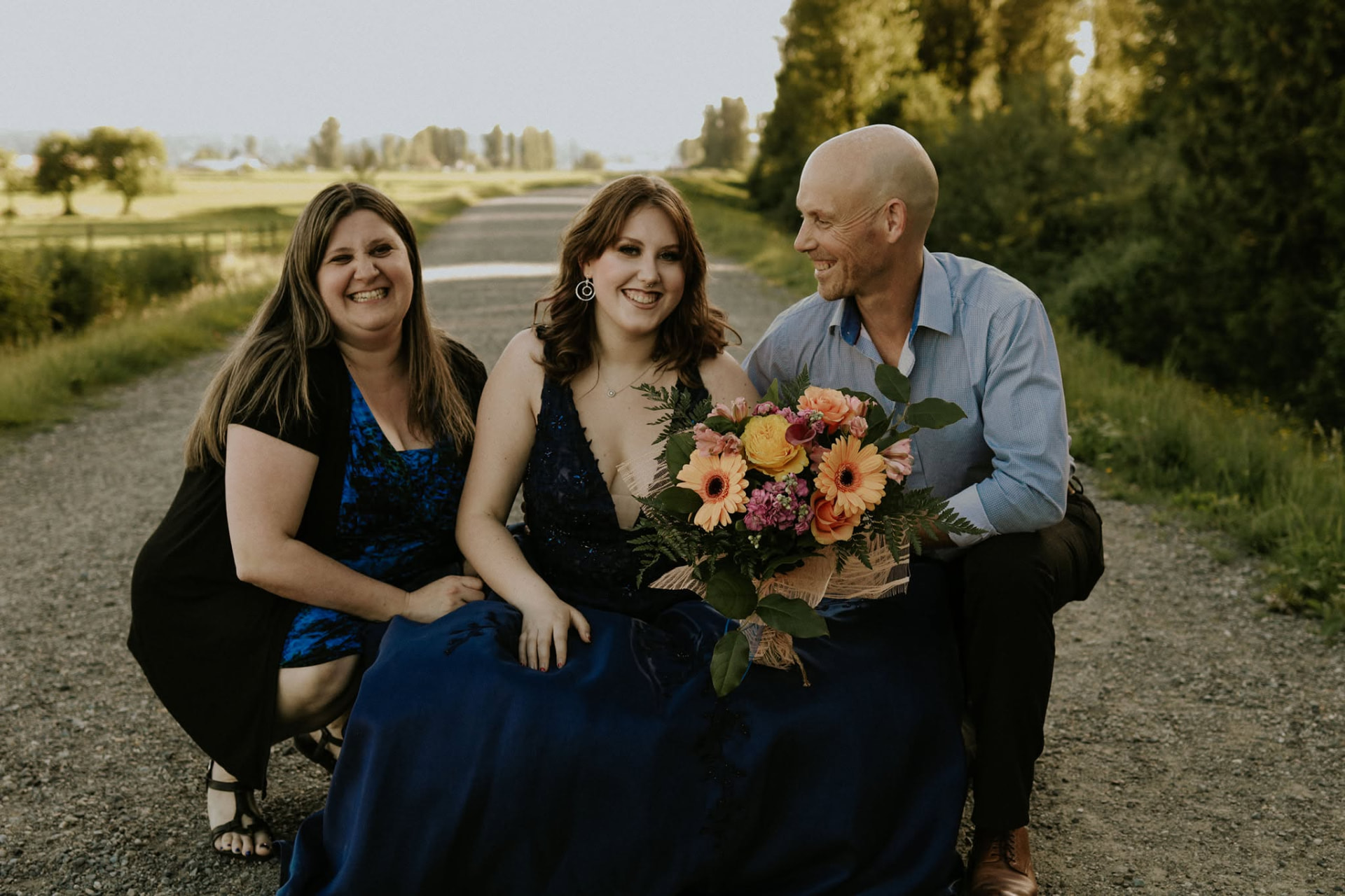 Graduate seated with her parents on a gravel lane at golden hour